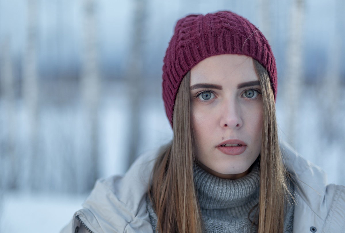 kobieta w wieku 35 plus z długimi włosami i w czapce stoi smutna na zewnątrz