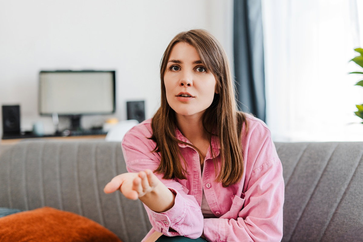 kobieta w wieku 30 plus w różowej koszuli siedzi zdziwiona i zdenerwowana na kanapie