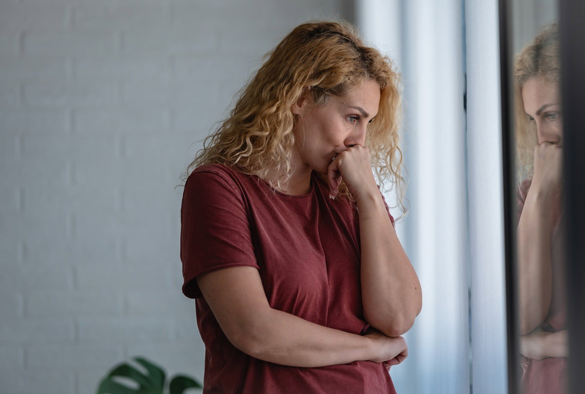 kobieta w wieku 35 plus z kręconymi włosami w miedzianym t-shircie stoi zmartwiona