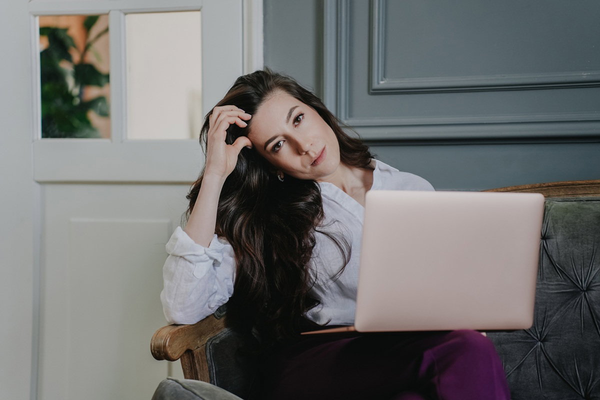 elegancka kobieta 30 plus siedzi na sofie z laptopem podłamana i smutna