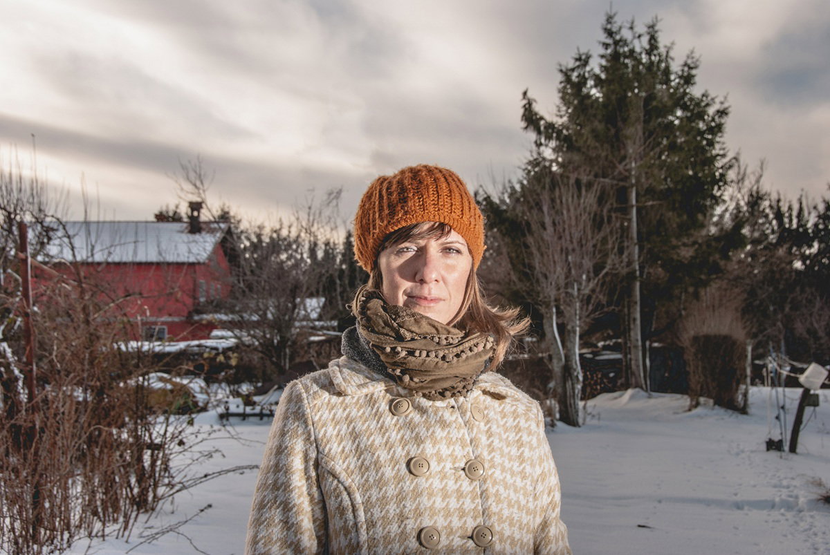 kobieta w wieku 40 plus w żółtej czapce stoi na zewnątrz na tle zaśnieżonego pejzażu smutna