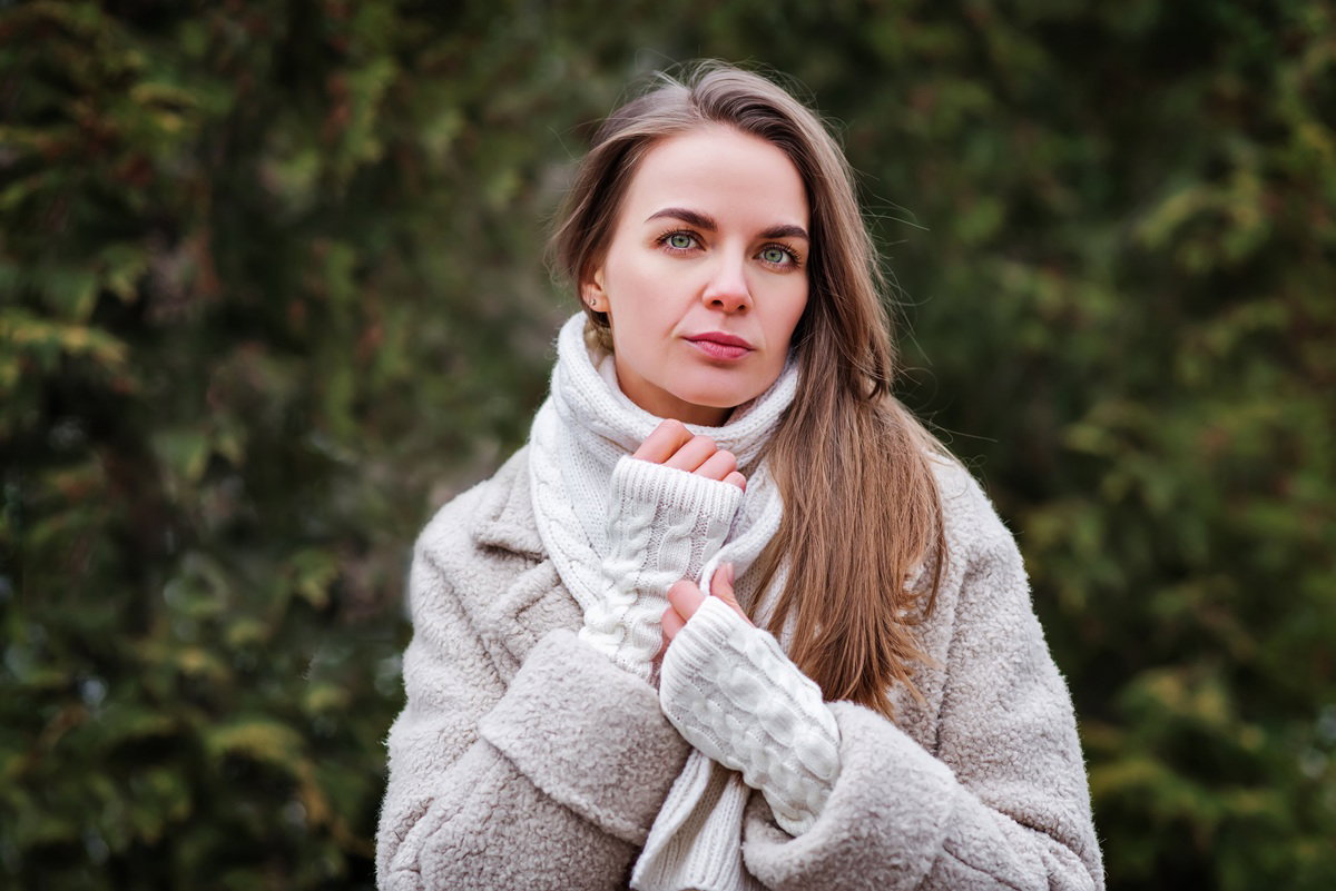 kobieta w wieku 35 plus w szalu i mitenkach patrzy smutno przed siebie stojąc na zewnątrz