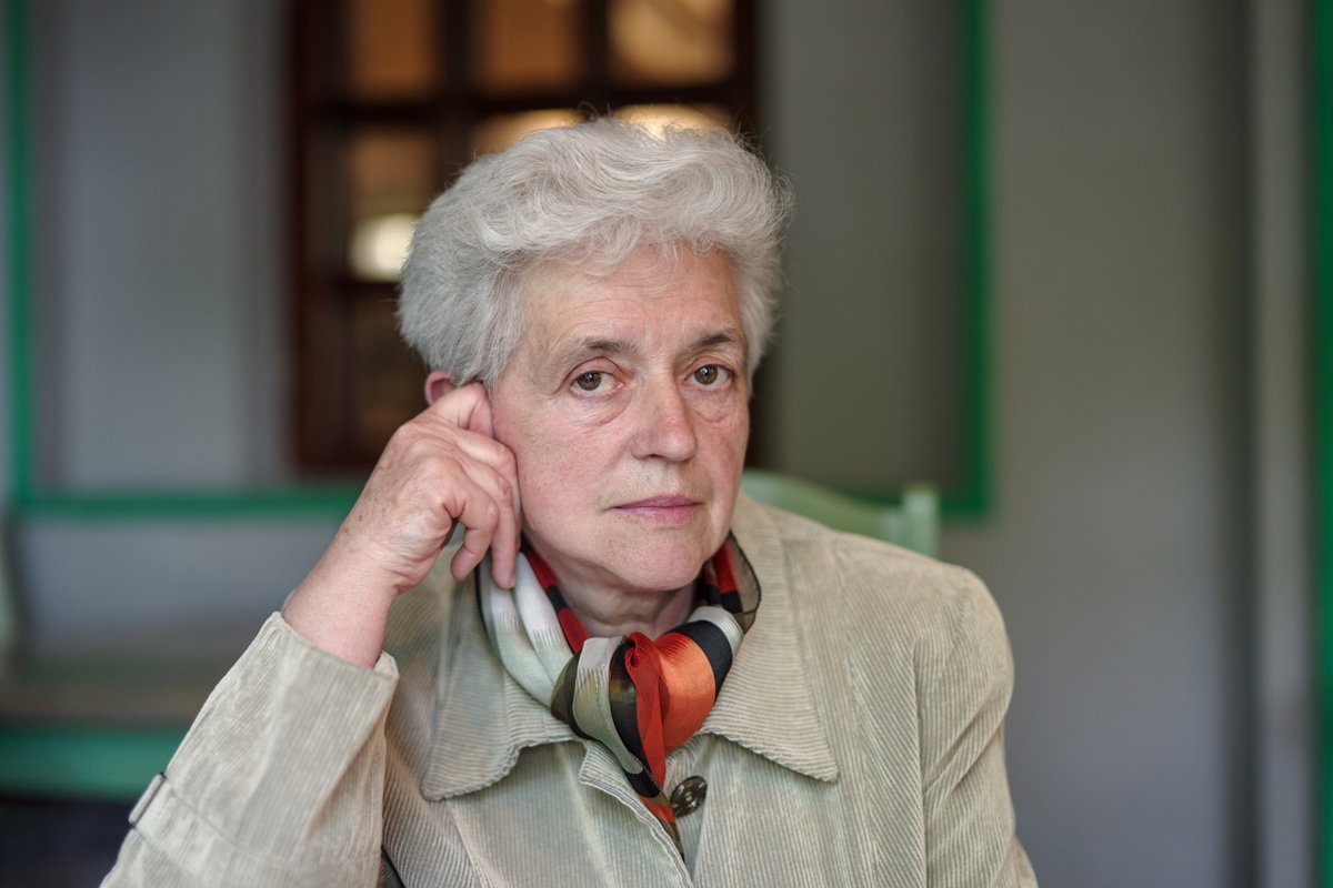 kobieta w wieku 65 plus z siwymi krótkimi włosami siedzi smutna i zamyślona