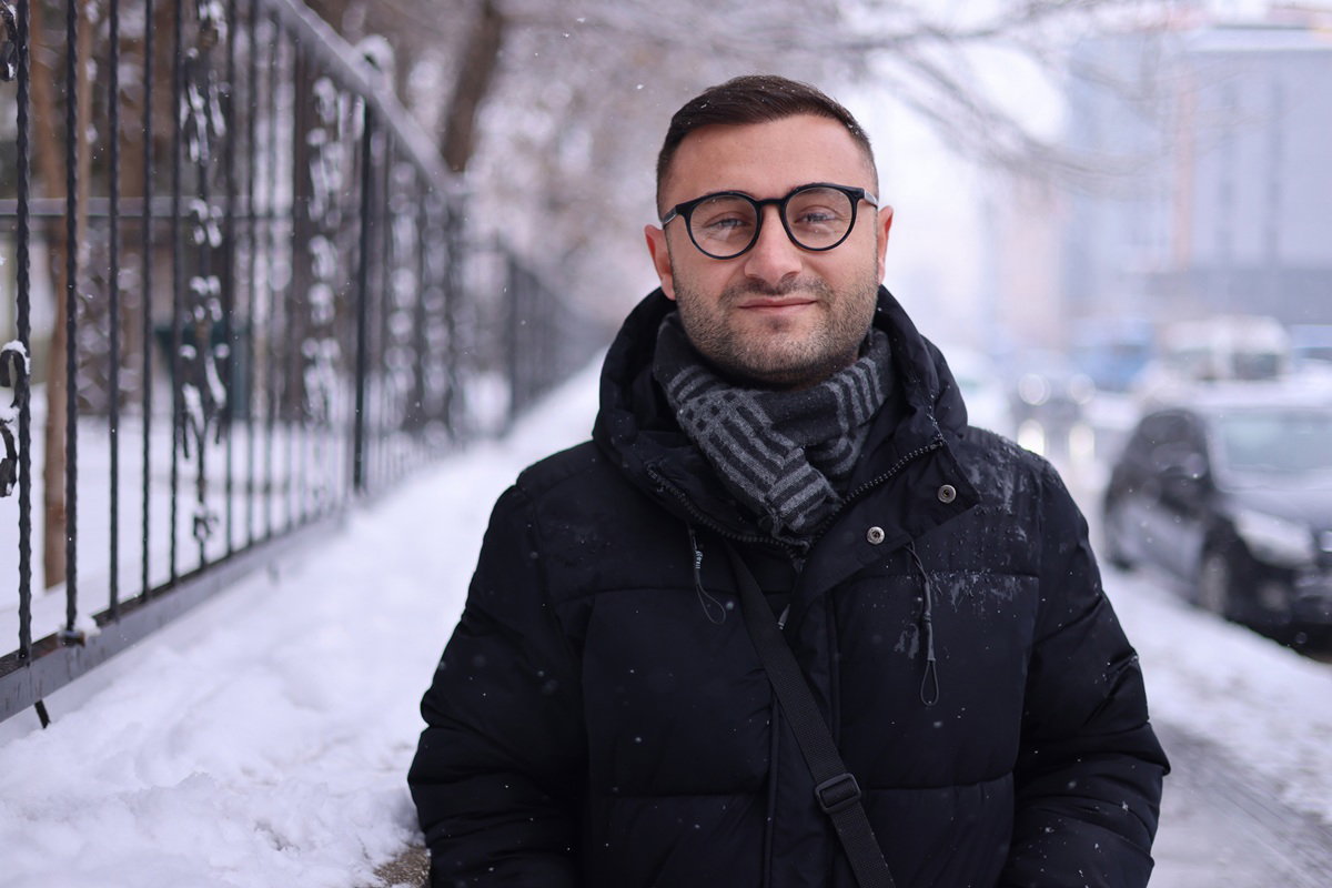 mężczyzna w wieku około 30 lat z zarostem i w okularach stoi na zaśnieżonej ulicy