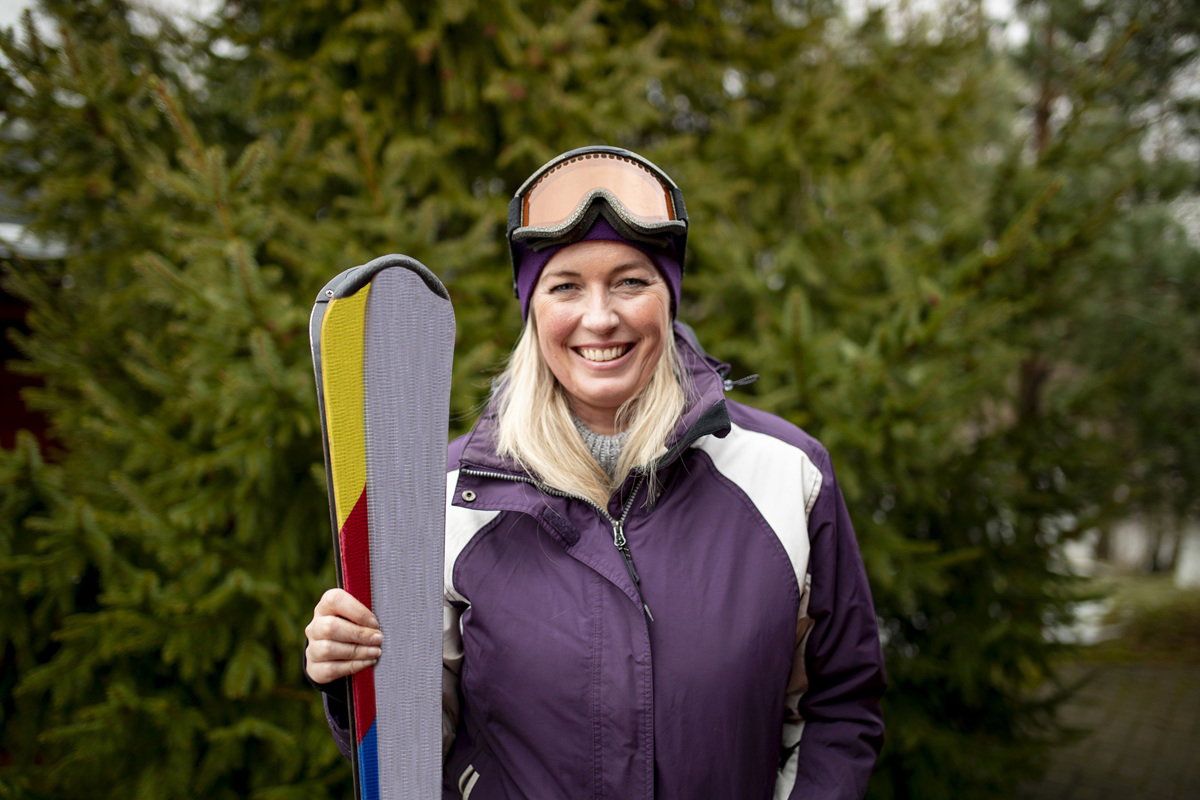 kobieta w wieku 40 plus w kurtce narciarskiej stoi z nartami i uśmiecha się szeroko