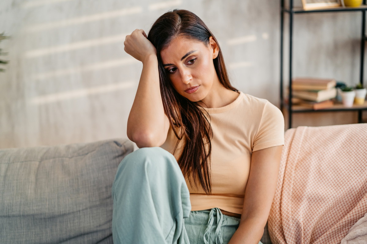 Sad Young Woman Sitting At Home On The Sofa