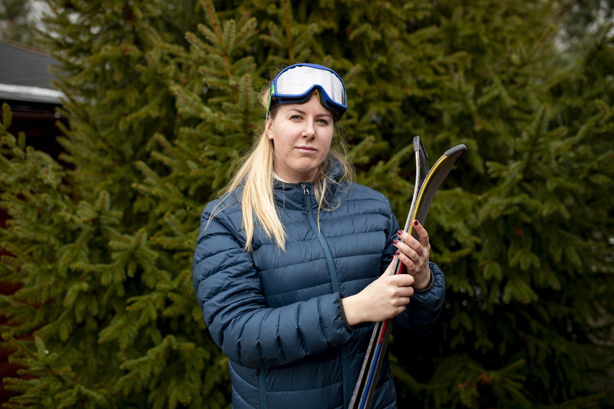 kobieta w wieku około 35 plus w kurtce puchowej trzyma narty i ma poważną minę