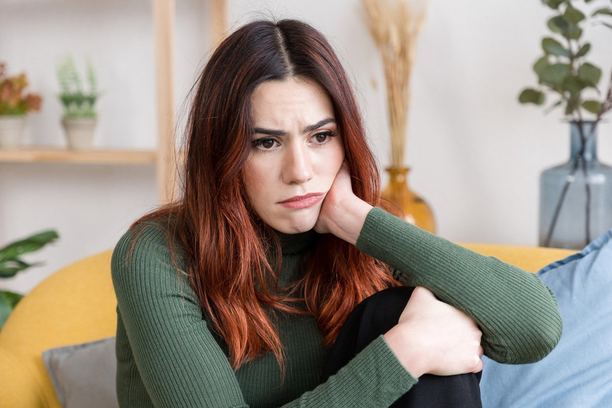kobieta w wieku 35 plus siedzi ze smutną miną w salonie zawiedziona