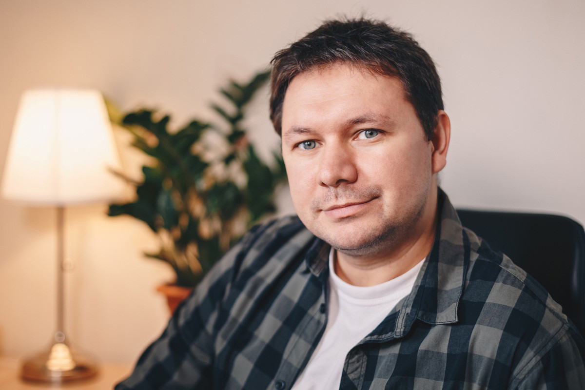 mężczyzna w wieku 35 plus w kracistej koszuli siedzi w fotelu i lekko się uśmiecha