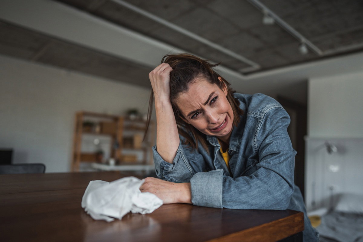 kobieta w wieku 25 plus w jeansowej kurtce siedzi przy stole i płacze zrozpaczona