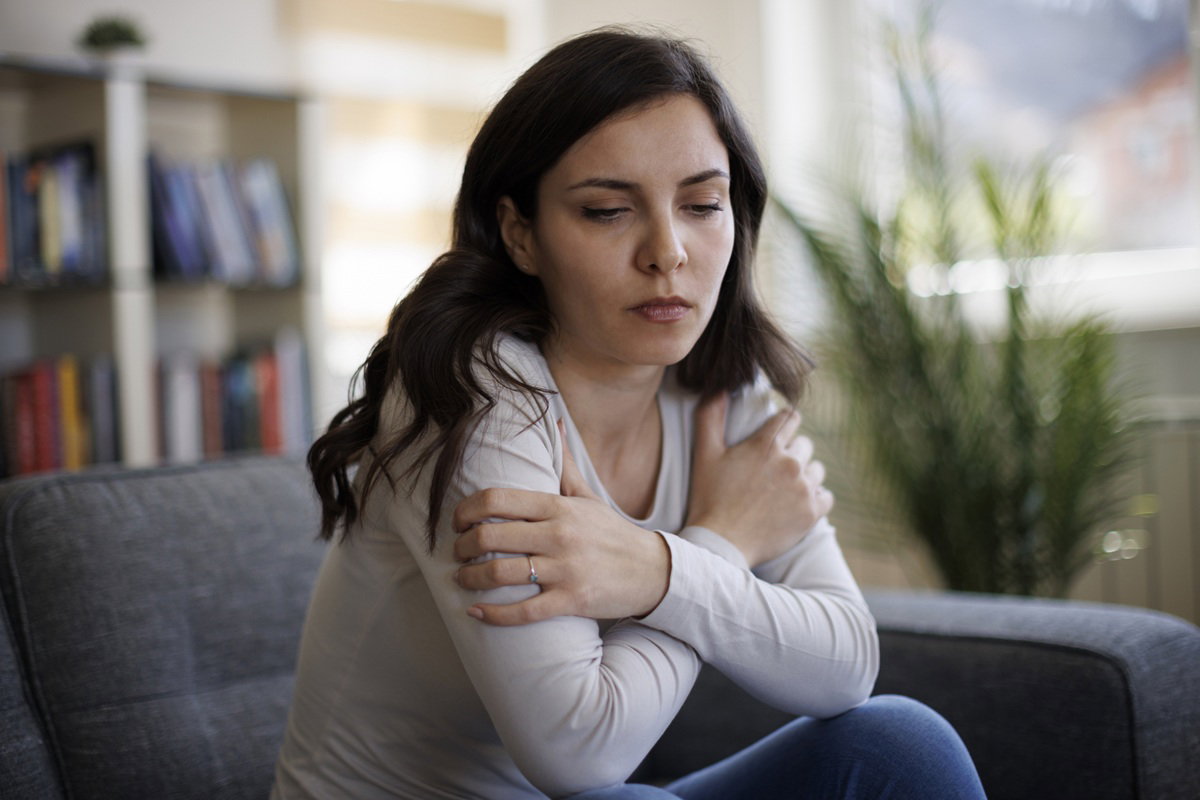 kobieta w wieku 30 plus siedzi na kanapie ze skrzyżowanymi ramionami załamana i smutna