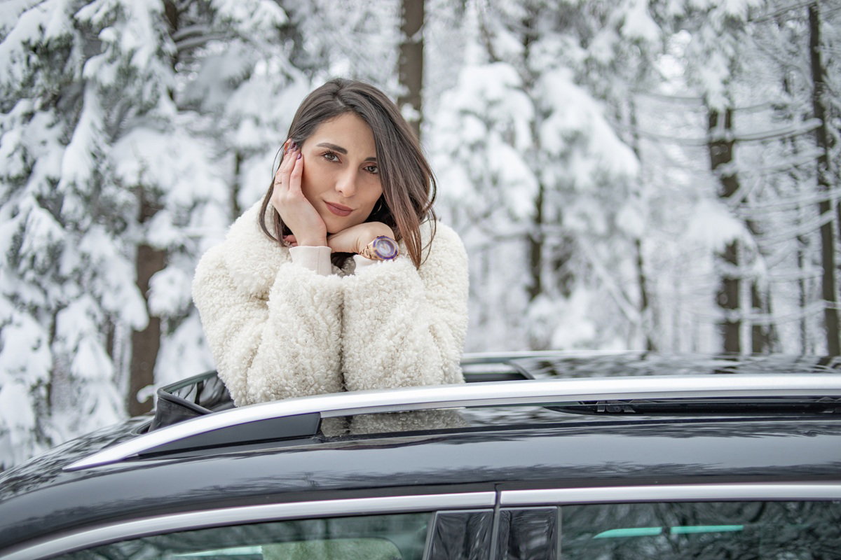 atrakcyjna kobieta w wieku 30 plus stoi przy samochodzie na tle zimowego pejzażu rozmarzona