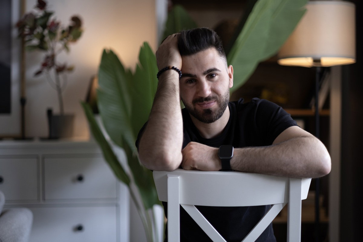 mężczyzna w wieku 30 plus z wąsami i brodą siedzi na krześle i uśmiecha się zdziwiony