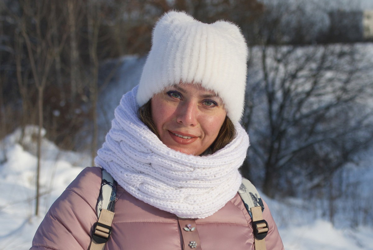 kobieta w wieku 35 plus w białej czapie i kominie stoi na zewnątrz z kpiącym uśmiechem