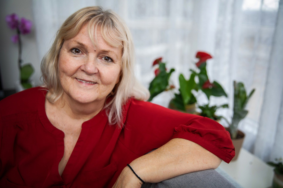 kobieta w wieku 60 plus z jasnymi włosami w czerwonej bluzce siedzi uśmiechnięta w fotelu