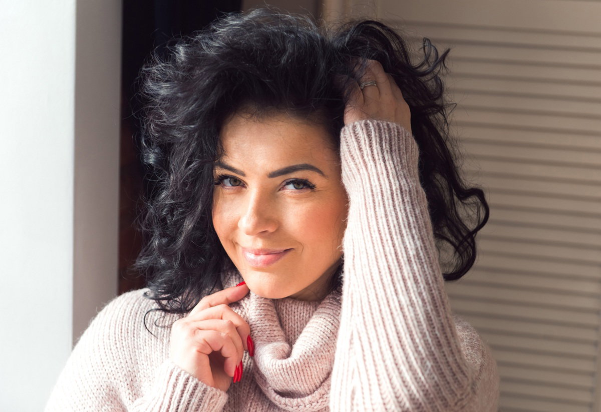 kobieta w jasnym swetrze w wieku 25 plus z ciemnymi włosami uśmiecha się zalotnie