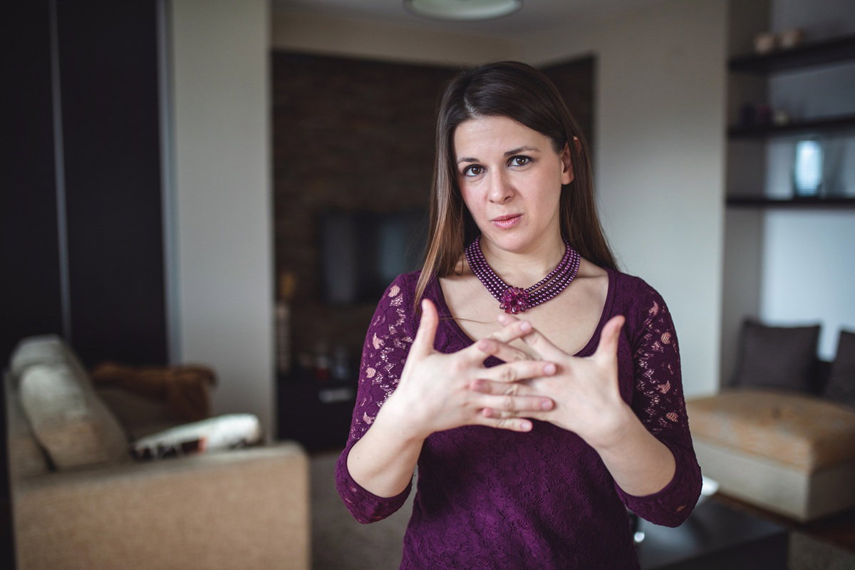 kobieta w wieku 30 plus w fioletowej sukience i naszyjniku stoi ze splecionymi rękami w geście obronnym