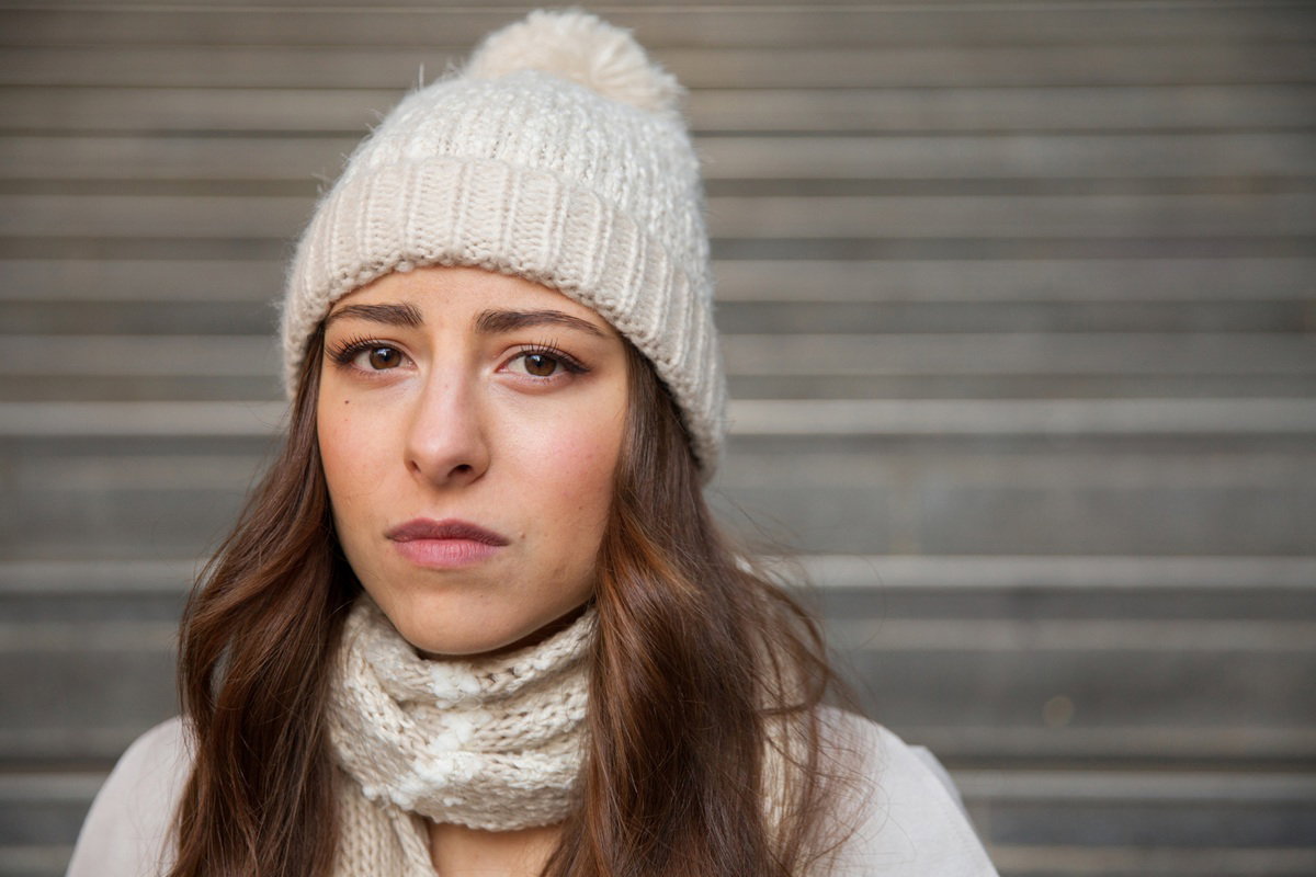kobieta w wieku 25 plus w jasnej czapce z pomponem stoi smutna i zamyślona