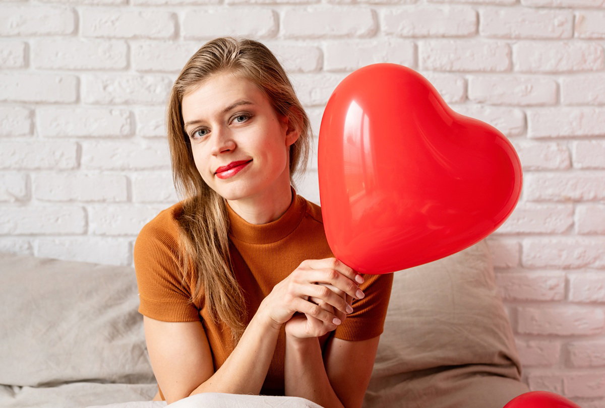 kobieta w wieku 25 plus siedzi z czerwonym balonikiem w rękach ze zdziwioną miną