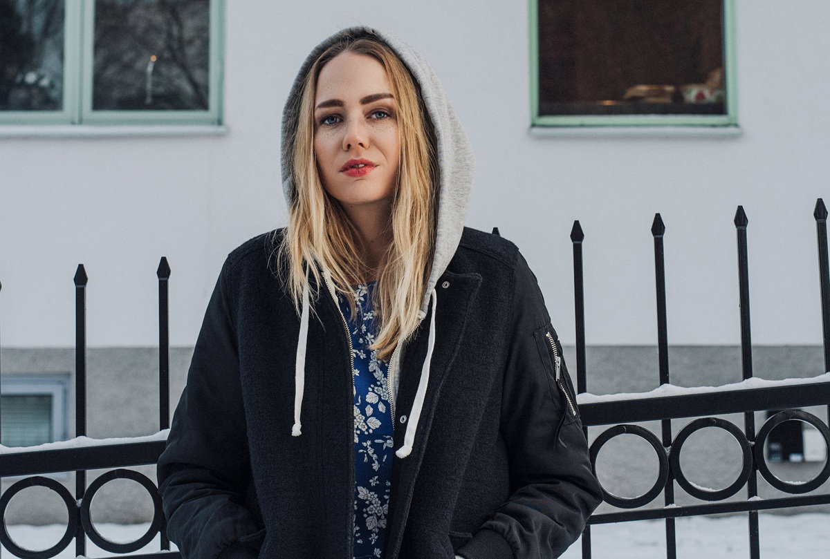 kobieta w wieku 25 plus w kurtce z kapturem stoi na tle ogrodzenia domu zdegustowana