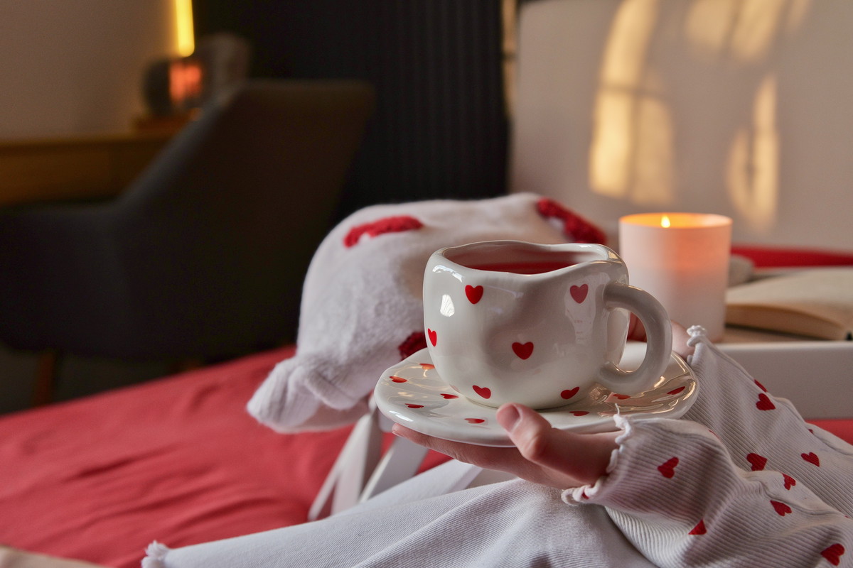 Cozy morning with a heart-themed mug of tea and a book by candlelight