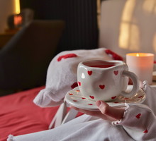 Cozy morning with a heart-themed mug of tea and a book by candlelight