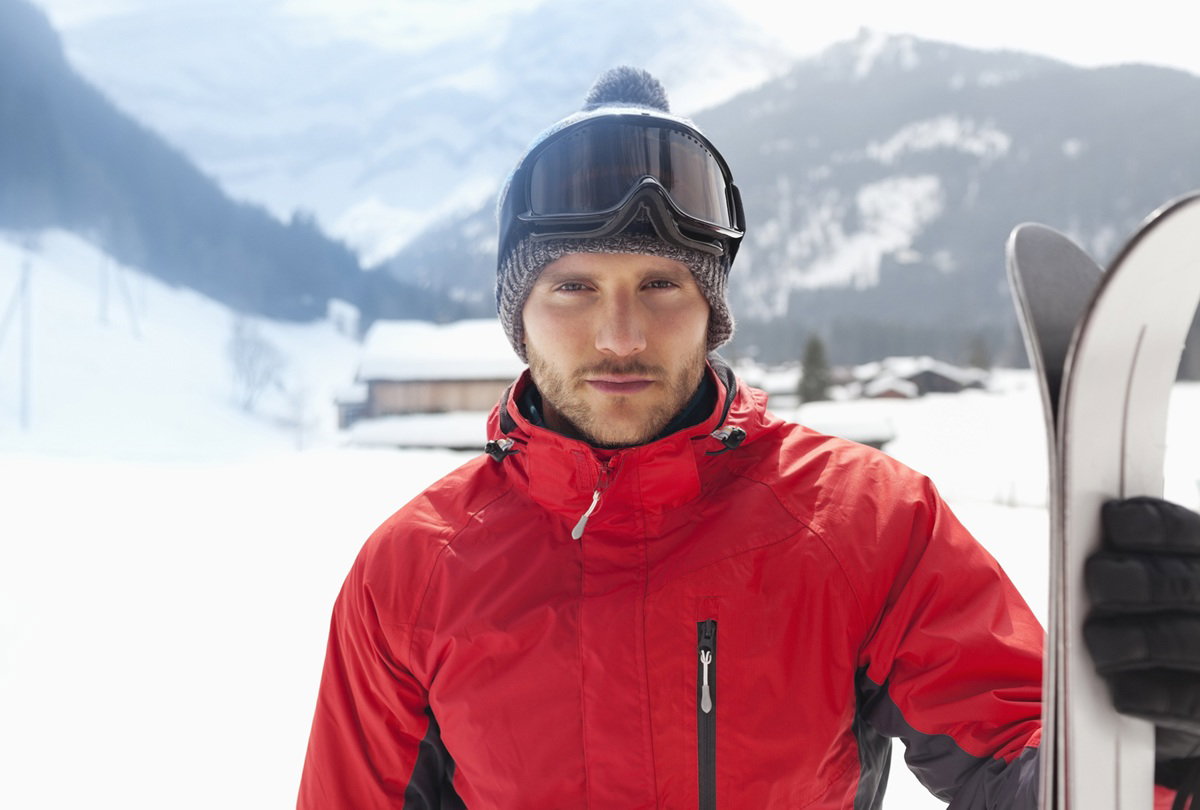 mężczyzna w wieku 30 plus w czerwonej kurtce z nartami na stoku stoi zamyślony i smutny