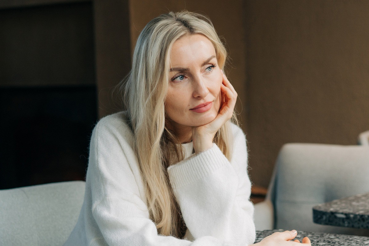 kobieta blondynka w wieku 35 plus w jasnym swetrze siedzi zamyślona i smutna w kawiarni