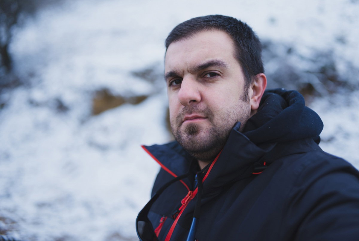 mężczyzna w wieku 30 plus z zarostem i ciemnymi włosami stoi na tle zimowego pejzażu zniesmaczony