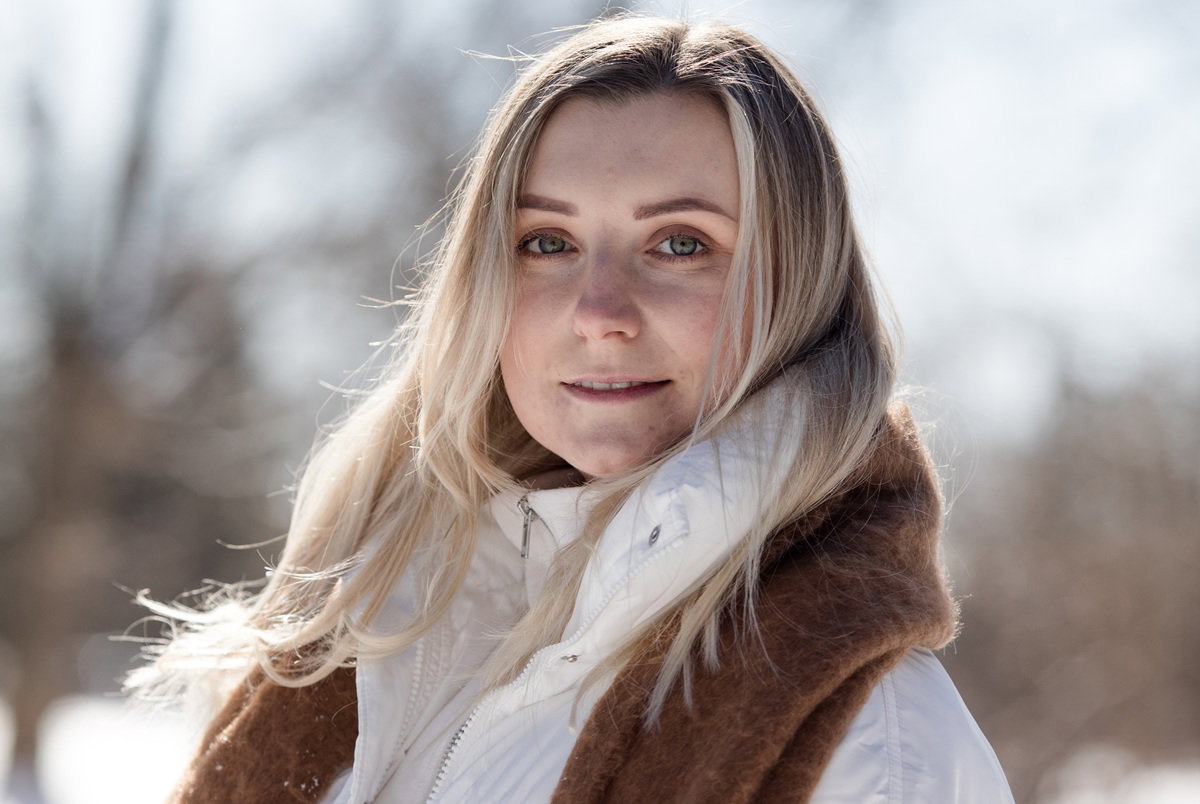 kobieta w wieku 35 plus blondynka z karmelowym szalem i w białej kurtce stoi na zewnątrz z poważną miną