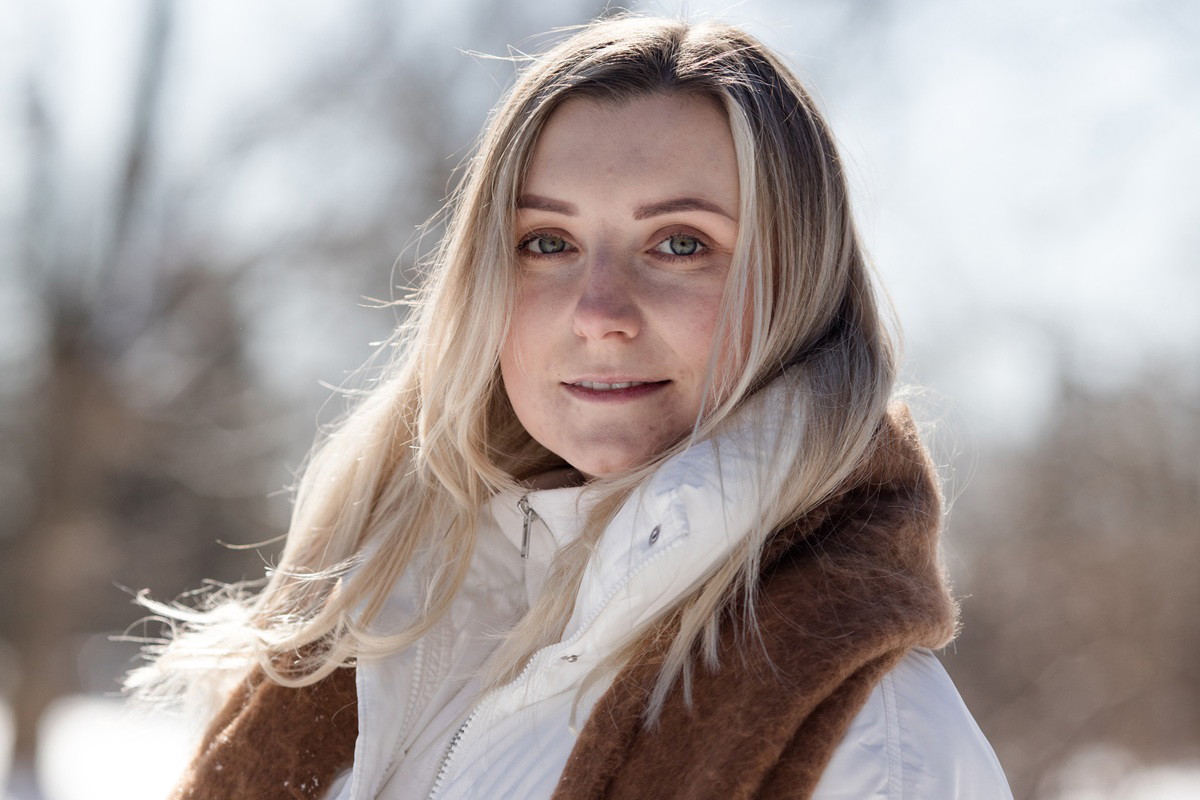 kobieta w wieku 35 plus blondynka z karmelowym szalem i w białej kurtce stoi na zewnątrz z poważną miną