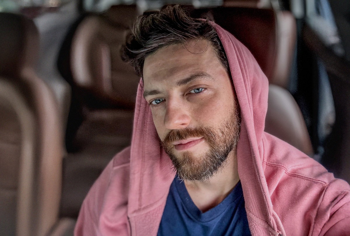 mężczyzna w wieku 35 plus w różowej bluzie siedzi w samochodzie podłamany