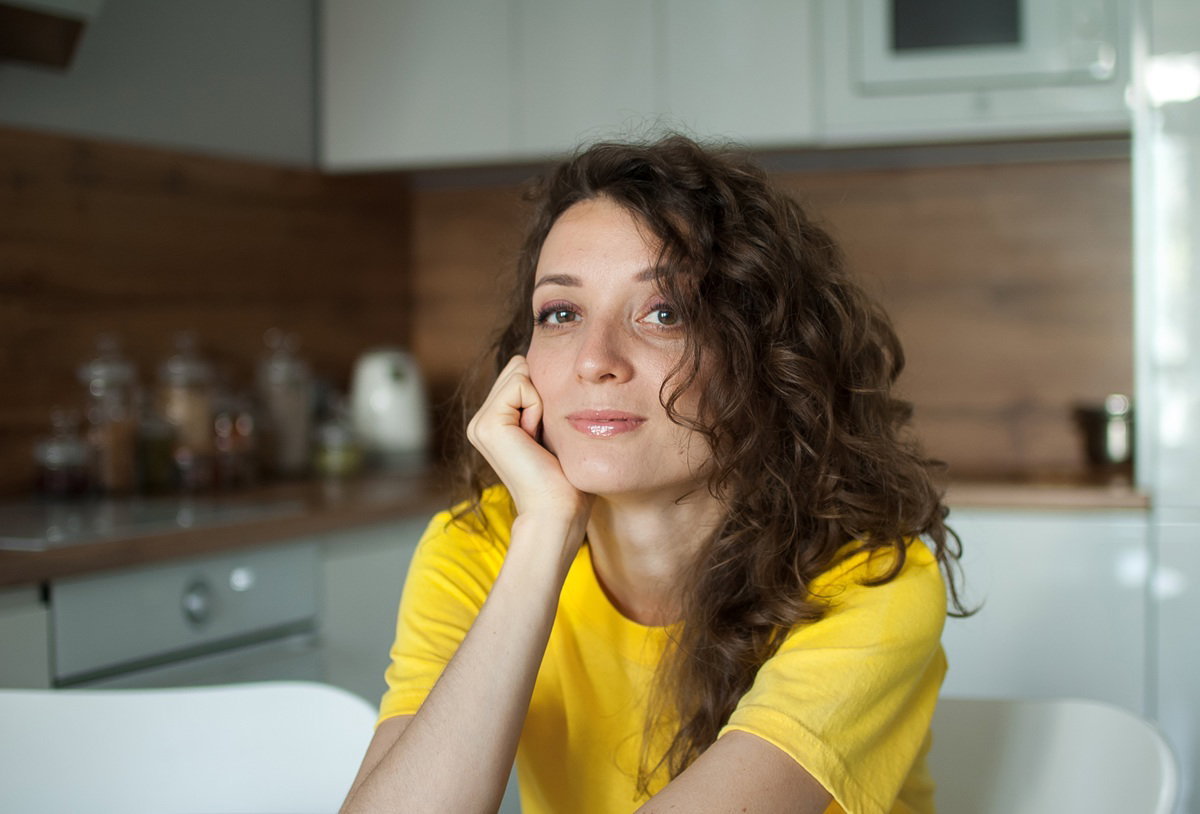 kobieta w wieku 35 plus w żółtym t-shircie siedzi w kuchni zamyślona
