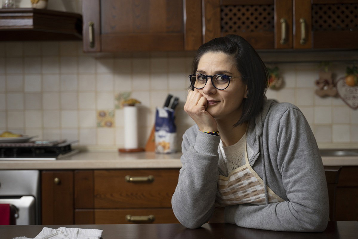 kobieta w wieku 30 plus w okularach siedzi w kuchni i lekko się uśmiecha zażenowana