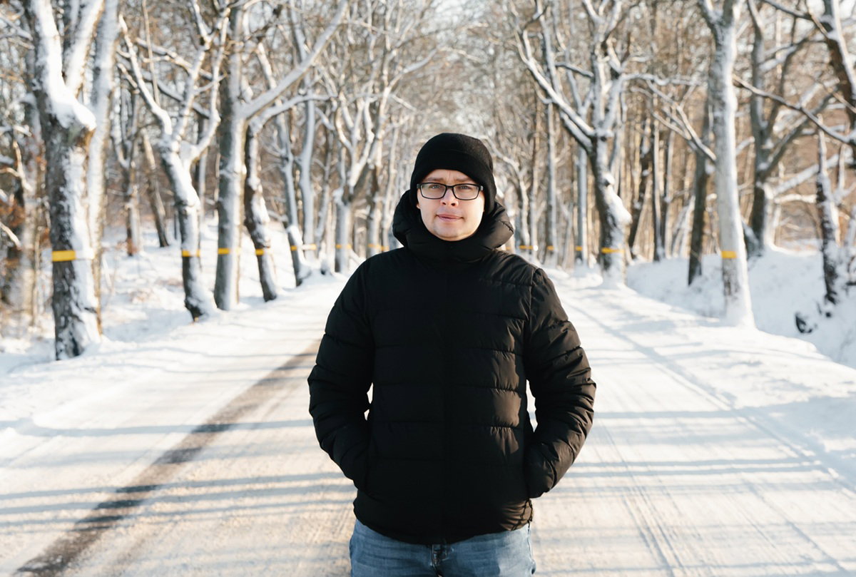 mężczyzna w wieku 35 plus w okularach i w czarnej kurtce soi na zaśnieżonej drodze zmartwiony