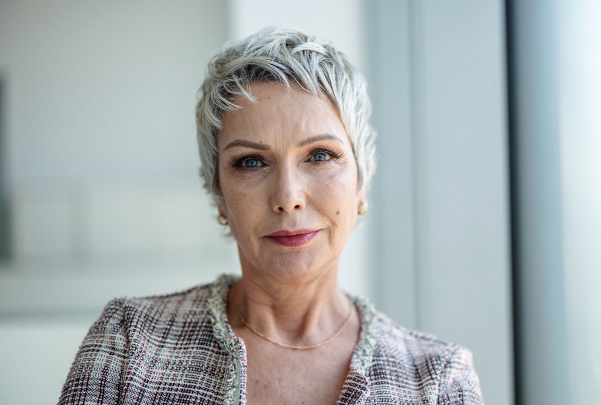 kobieta w wieku 55 plus z krótkimi włosami w żakiecie siedzi z poważną miną