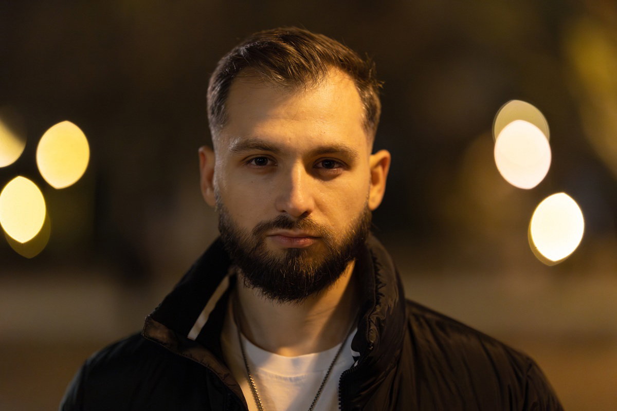 mężczyzna w wieku 30 plus z wąsami i brodą stoi na zewnątrz z poważną miną