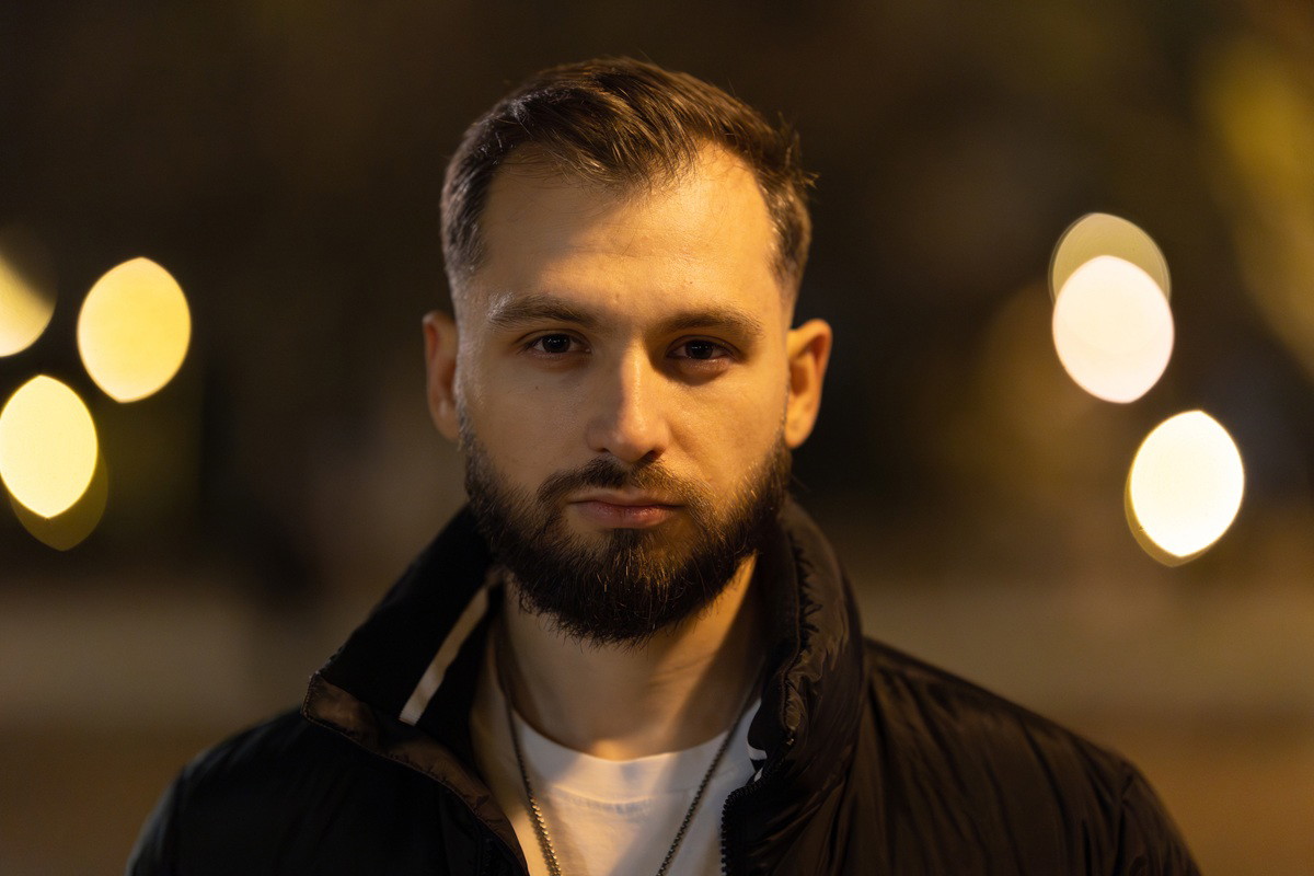mężczyzna w wieku 30 plus z wąsami i brodą stoi na zewnątrz z poważną miną