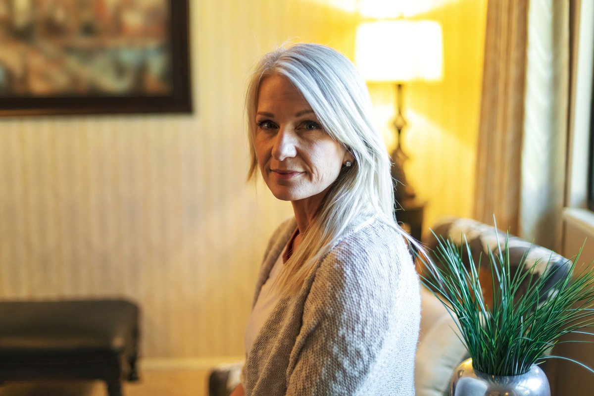 kobieta w wieku 40 plus jasne włosy siedzi w salonie zamyślona z nadzieją w oczach