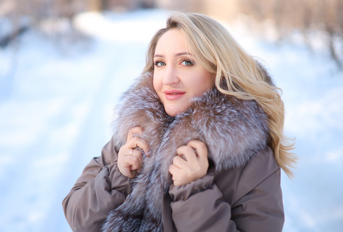 kobieta w wieku 35 plus blondynka stoi na tle zimowego pejzażu z zalotnym spojrzeniem