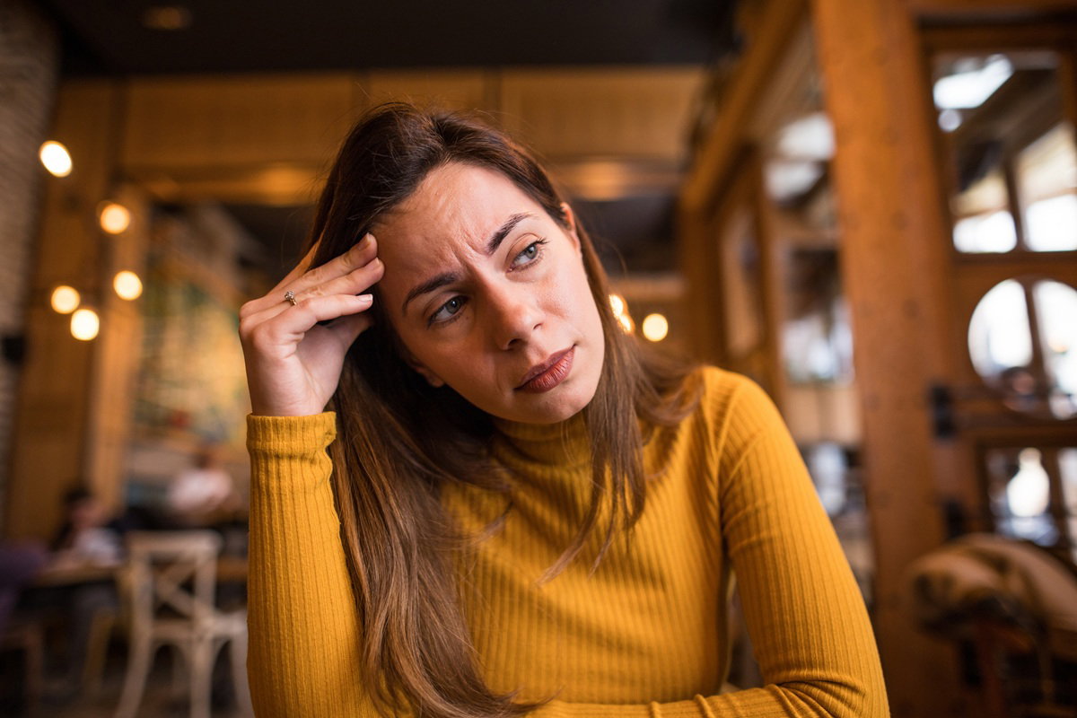 kobieta w wieku 30 plus w żółtej bluzce siedzi załamana w kawiarni