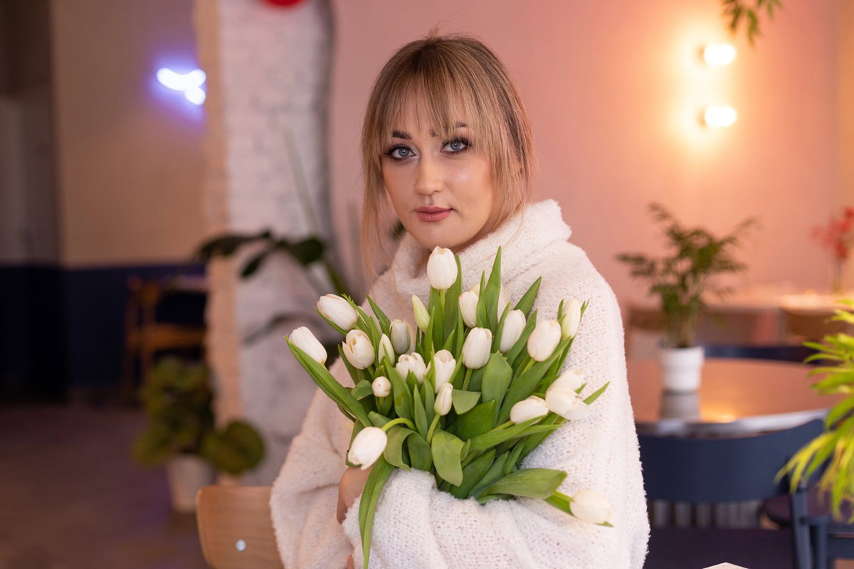 kobieta w wieku 30 plus blondynka z bukietem białych tulipanów stoi z poważną miną