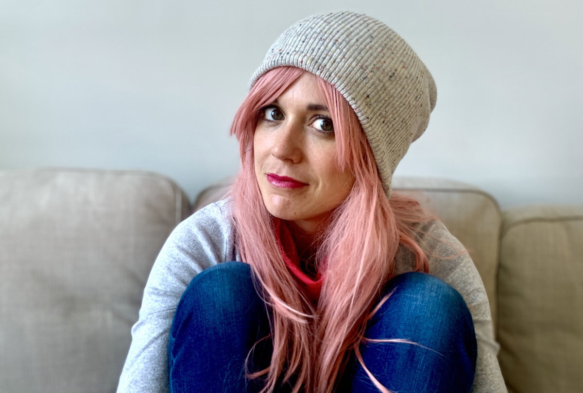 kobieta w wieku 25 plus z różowymi włosami w czapce siedzi na kanapie zawiedziona