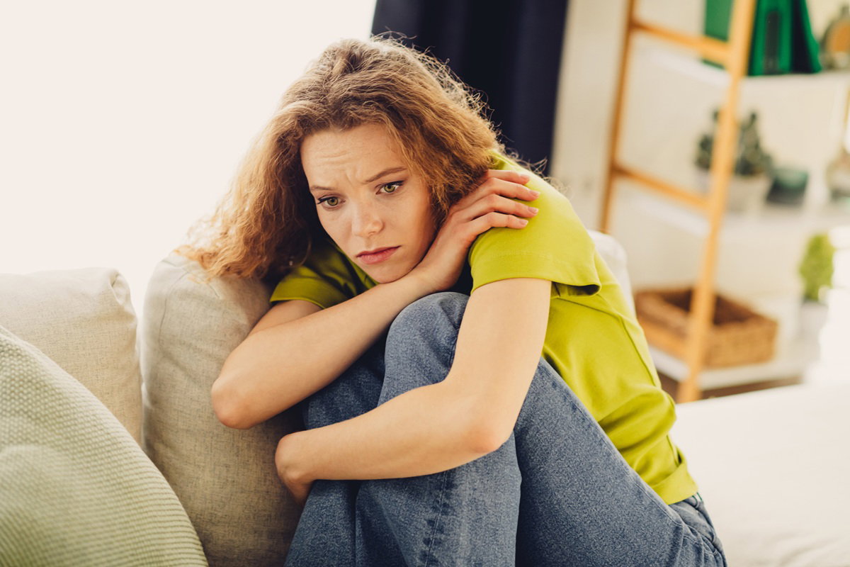 kobieta w wieku 25 plus z kręconymi rudymi włosami siedzi na kanapie załamana