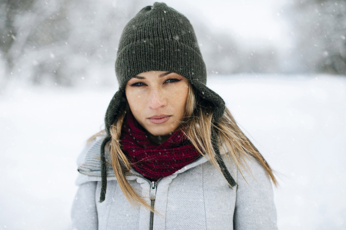 kobieta w wieku 35 plus w czapce stoi na tle zimowego pejzażu z poważną miną