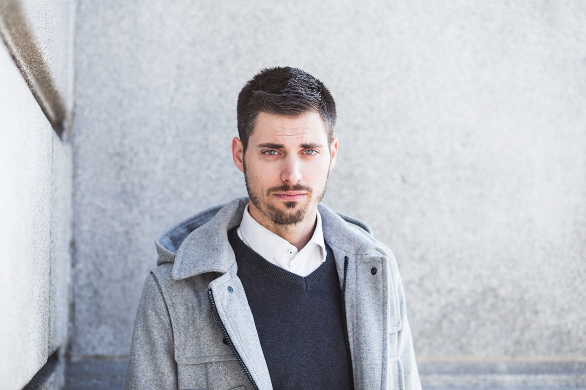 mężczyzna w wieku 25 plus w szarej kurtce stoi na tle szarego muru zawiedziony