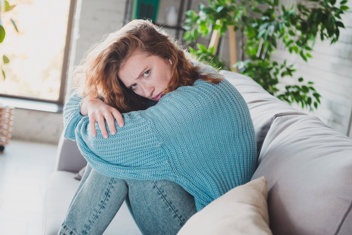 kobieta w wieku 25 plus w błękitnym swetrze siedzi na kanapie załamana