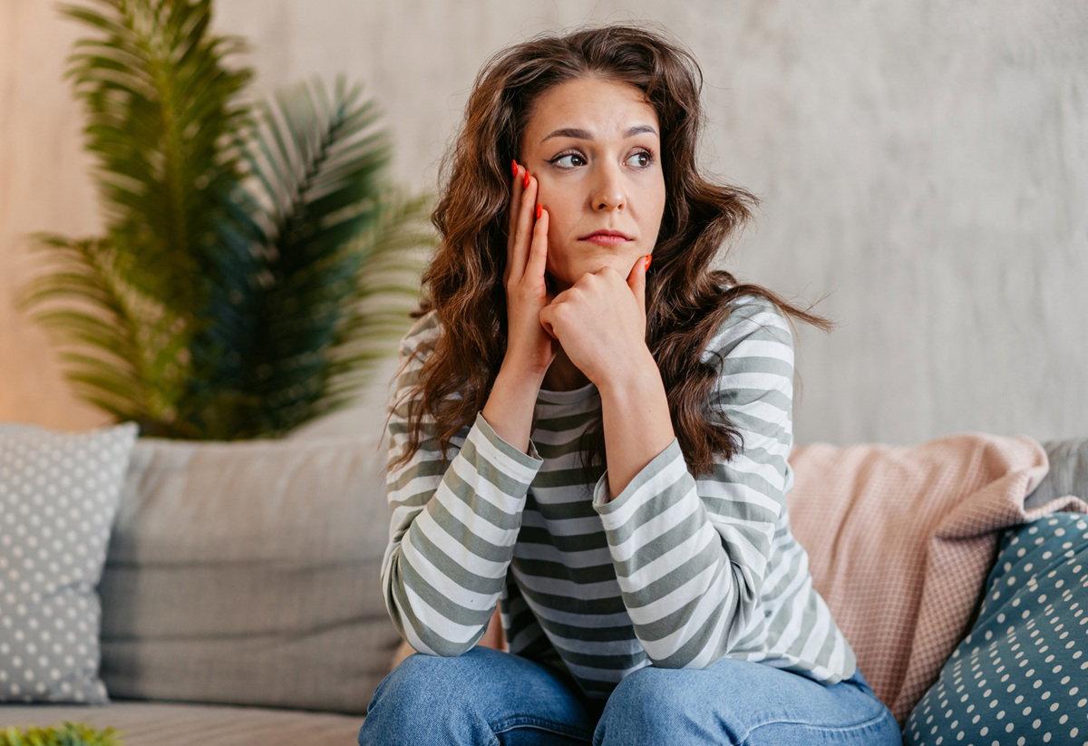 kobieta w wieku 30 plus w pasiastej bluzce siedzi na kanapie zamyślona