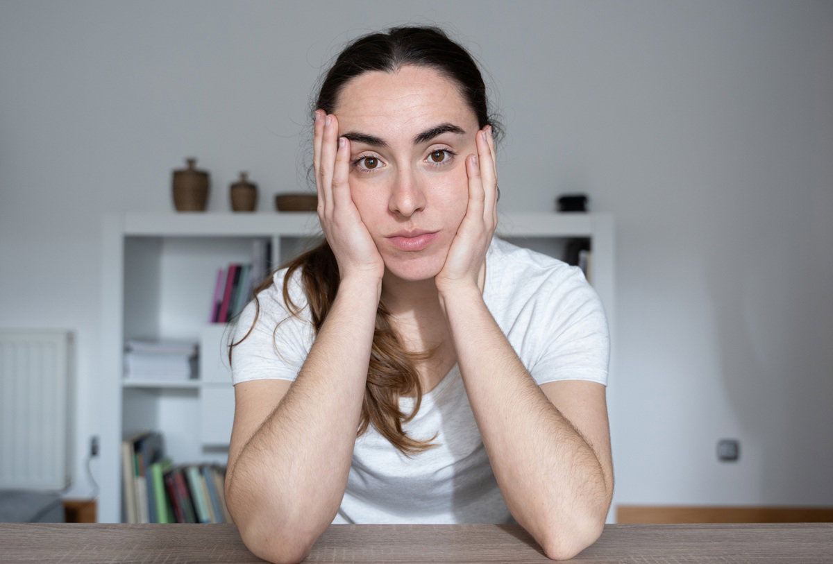 kobieta w wieku 30 plus z ciemnymi włosami siedzi przy stole zmartwiona na tle pokoju