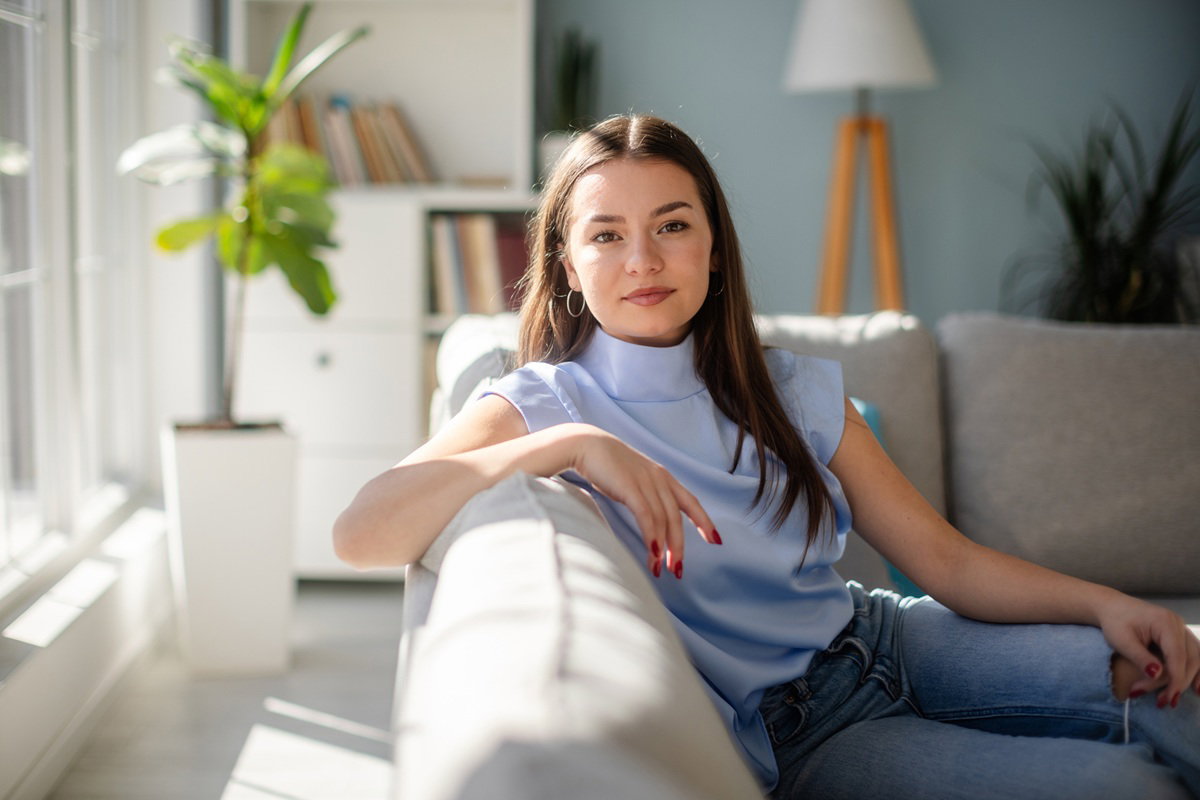 kobieta w wieku 30 plus siedzi na kanapie zamyślona i delikatnie się uśmiecha